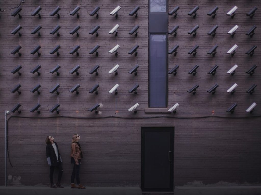 Parede coberta de câmeras de vigilância, com duas pessoas olhando para cima